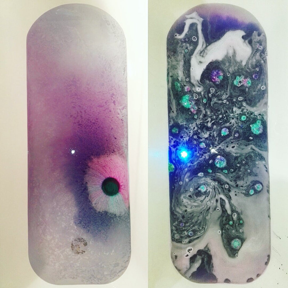 Side by side image of two baths, one with a dark purple bath bomb just put into the water and the second with the bath bomb dissolved, leaving a dark purple bath and a flashing light,