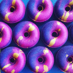 Purple and pink doughnut shaped bath bomb, with a gold stripe across the center hole.