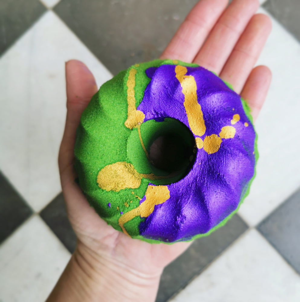 Bundt cake shaped bath bomb, bright green colour with a wide purple stripe and gold paint drizzle